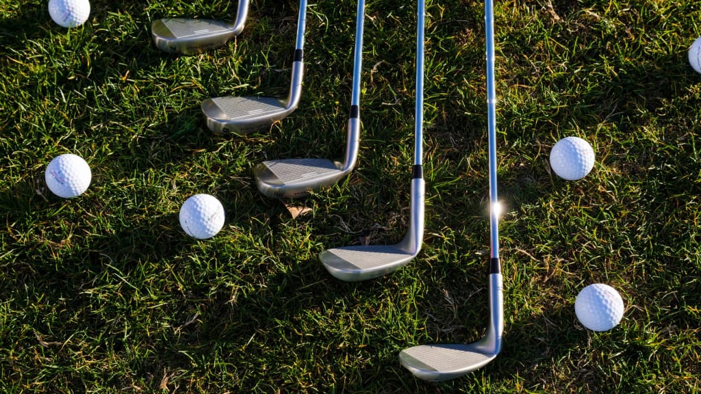 Golf clubs and golf balls are arranged on grass in a diagonal pattern.